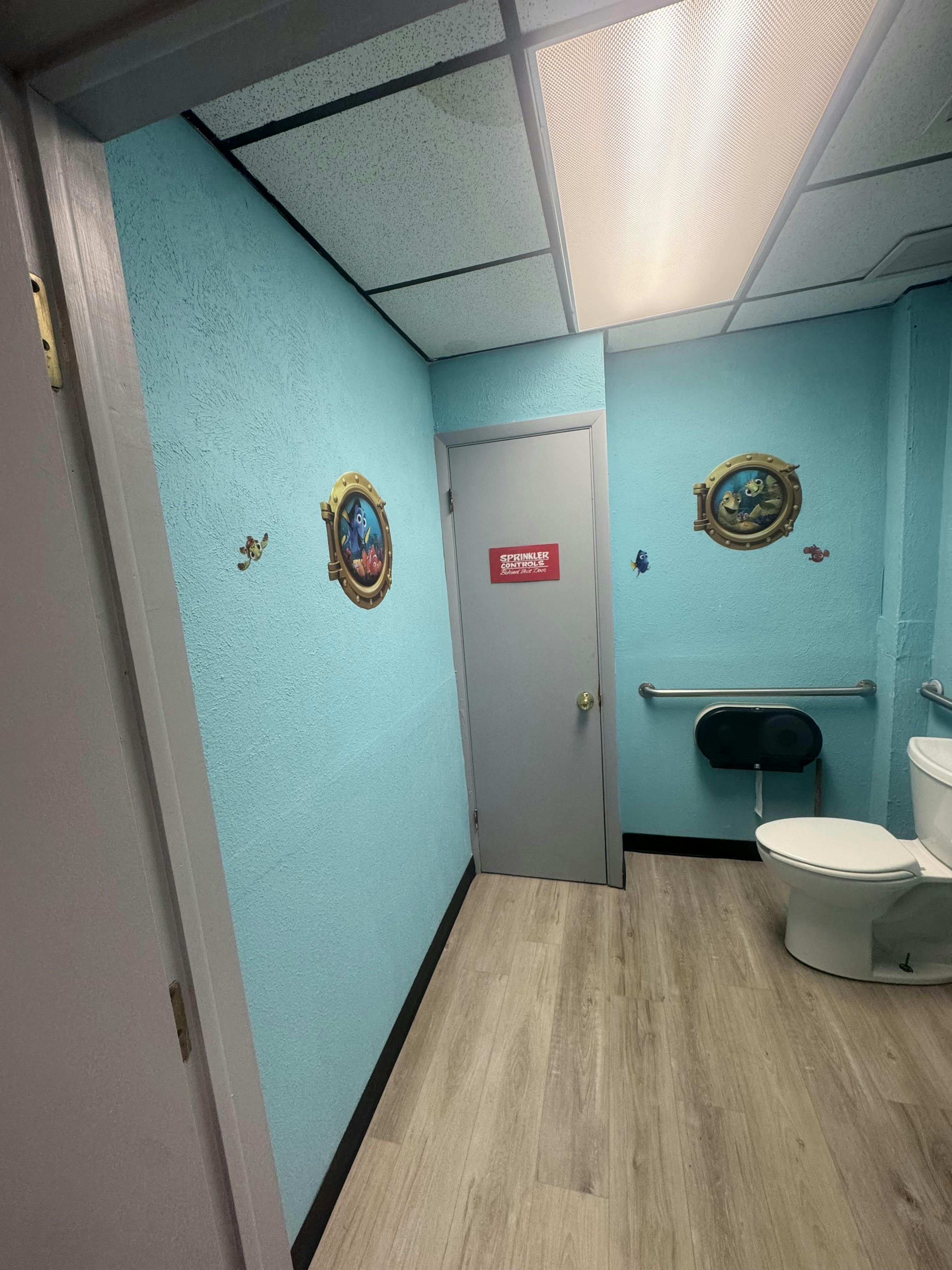 Public restroom with Finding Nemo wall decals and a sprinkler control sign