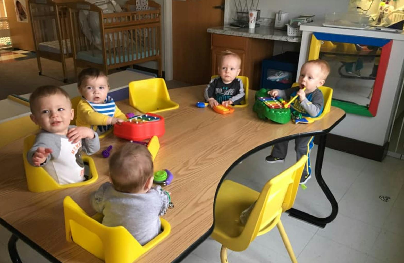 Multiple babies sitting at a table with toys