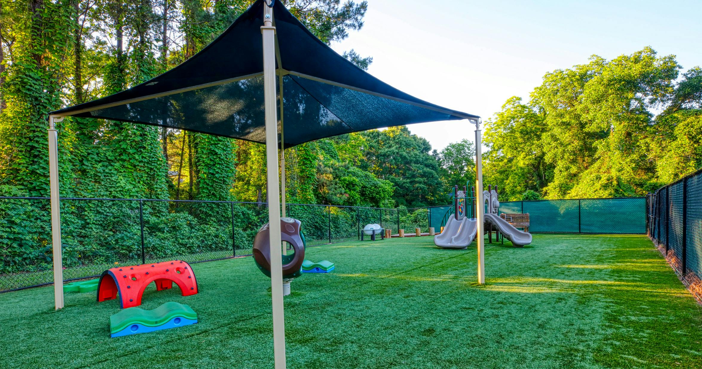 Playground with swings, slides, climbing structures on artificial turf, shaded by a canopy