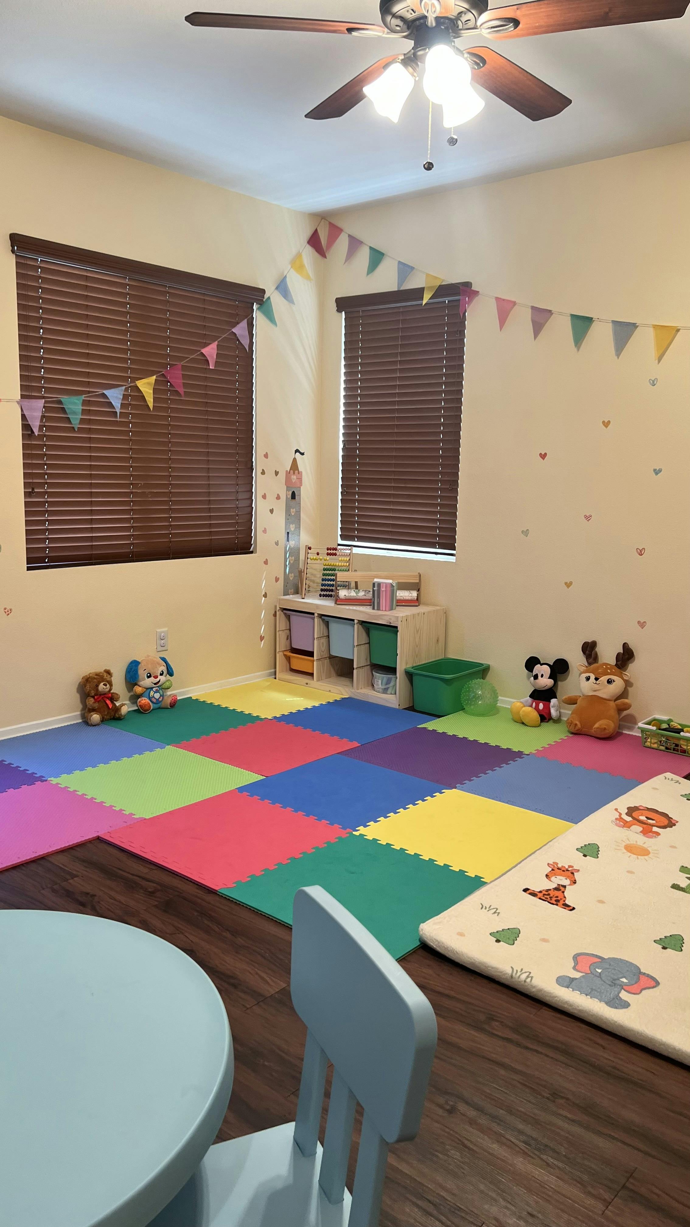 Playroom with colorful floor mats, stuffed animals, and small table and chair