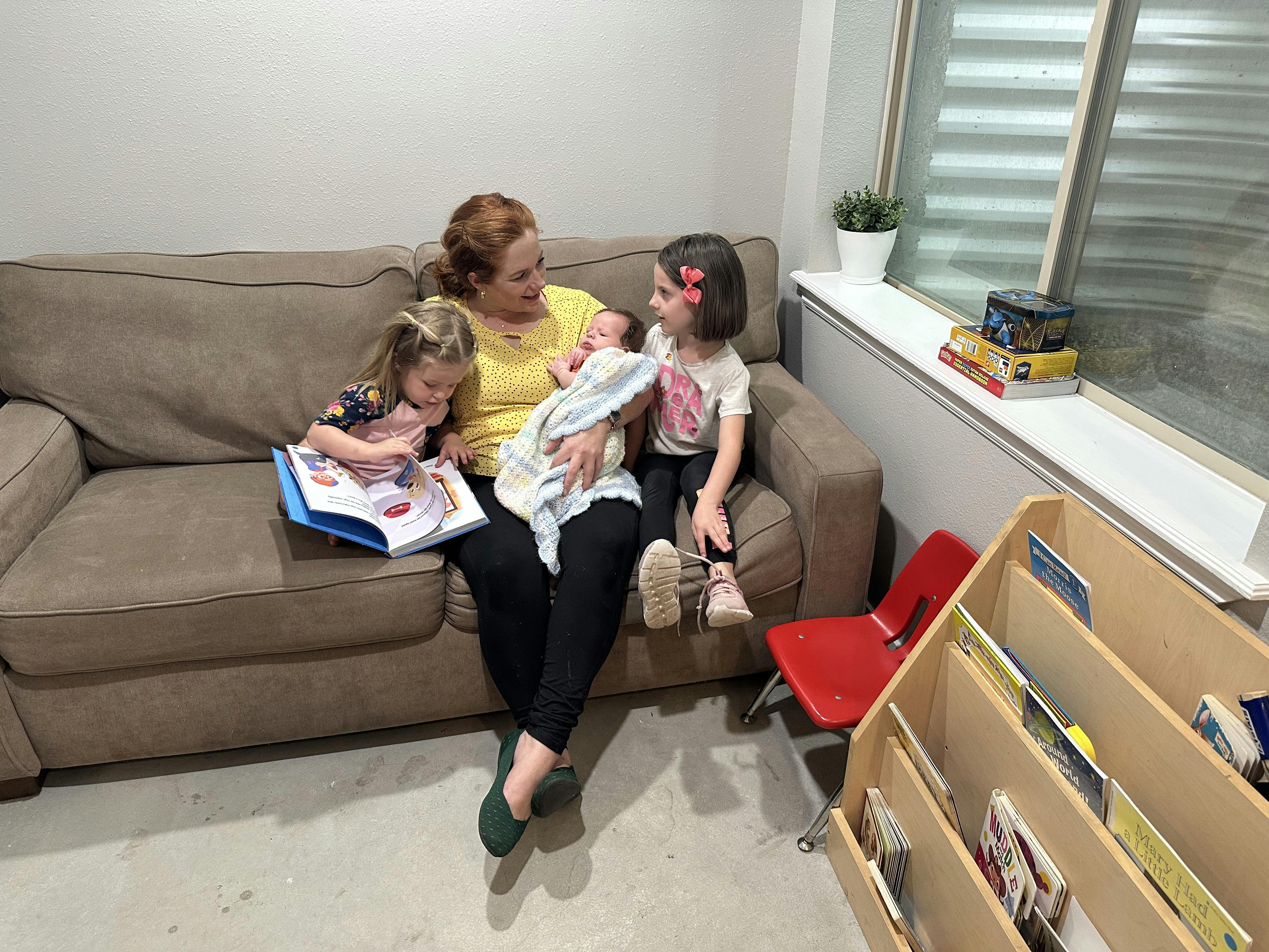 Person on couch holding infant, with two children beside them