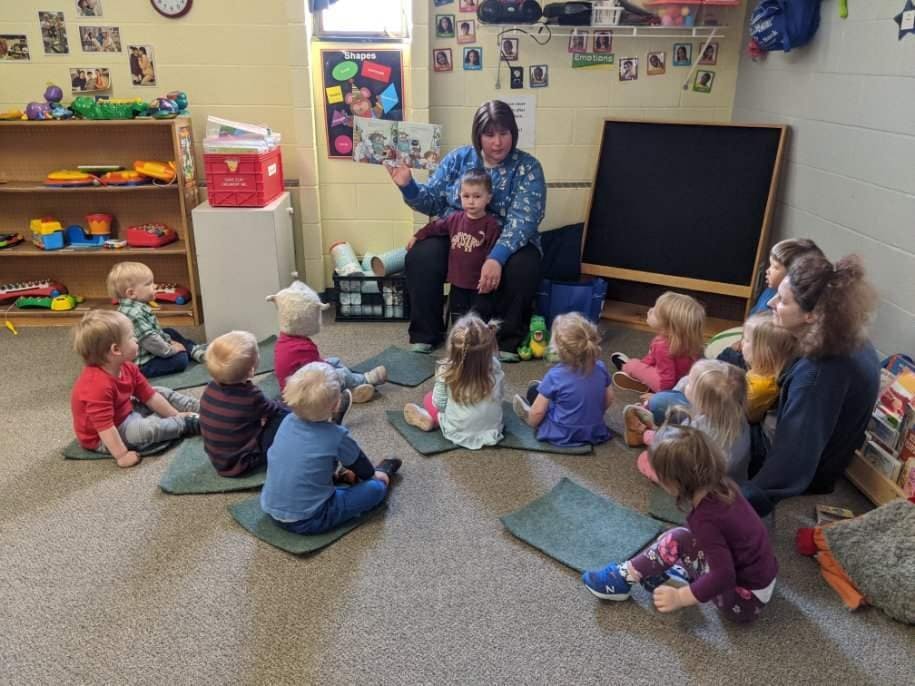 Person reading a book to a group of children in a classroom