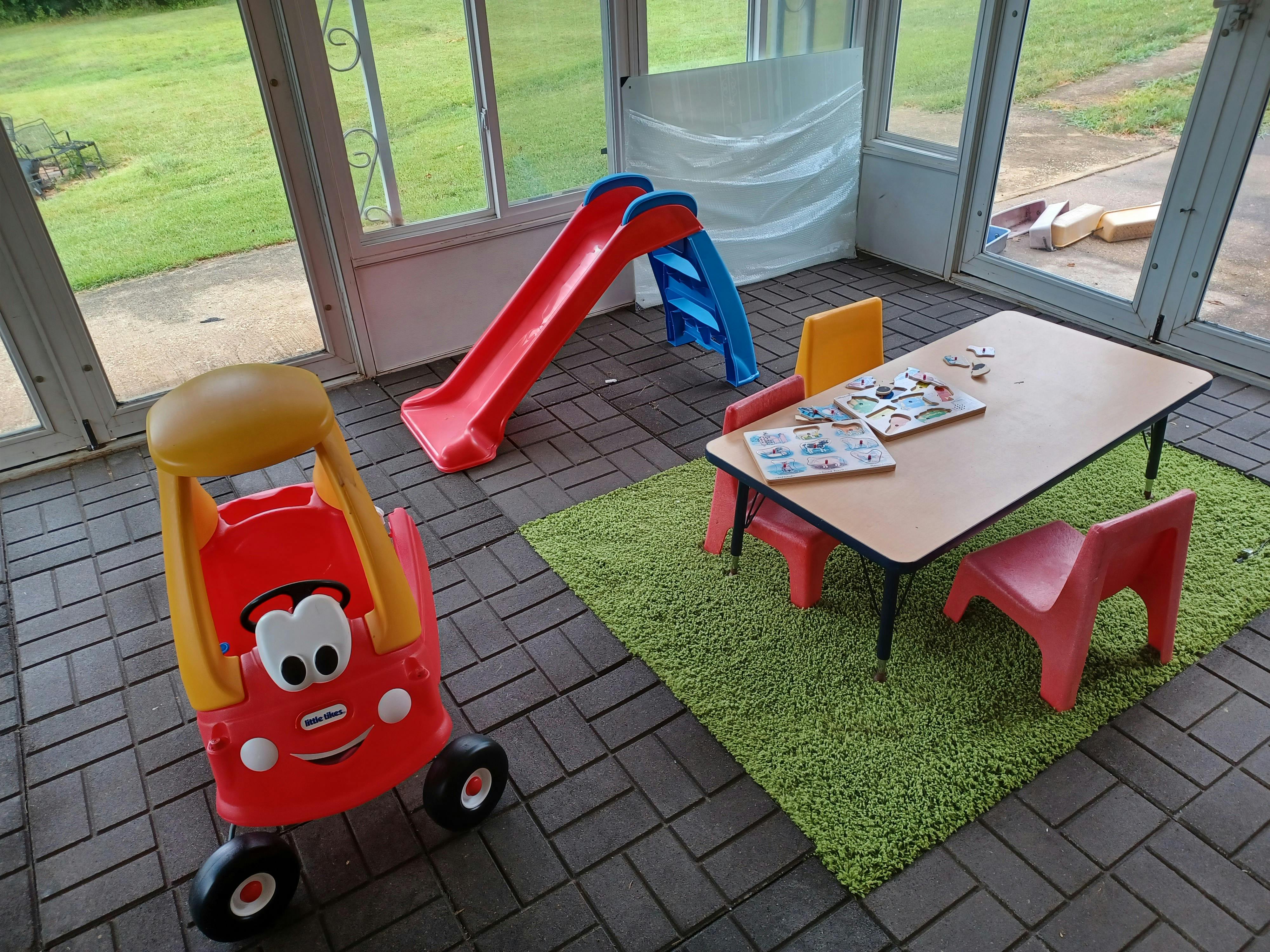 Toy car, slide, and table with chairs in a sunroom