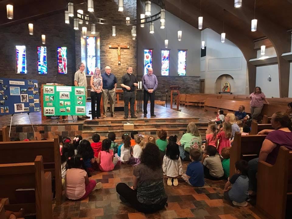 Adults standing on a stage in front of children sitting on the floor