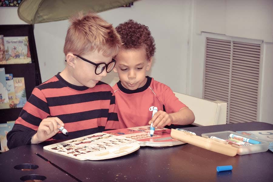 Two children drawing in books at a table