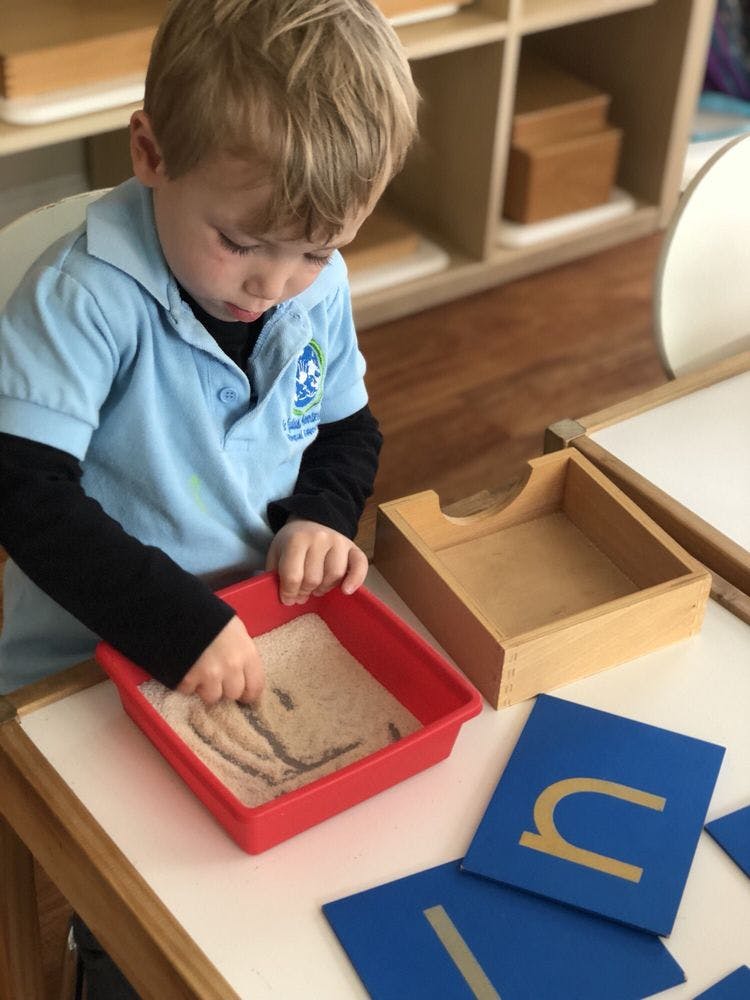 Child tracing letters in a sand tray