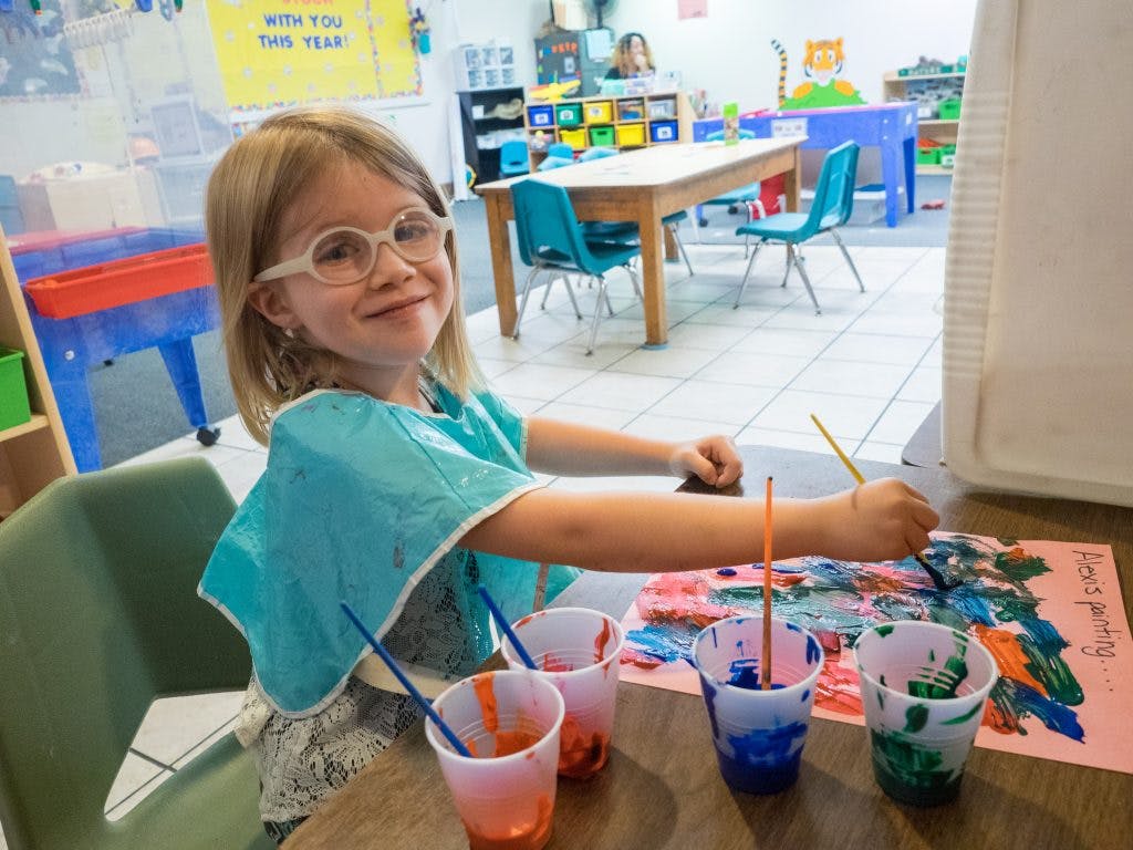 Child in glasses painting at a table in a classroom
