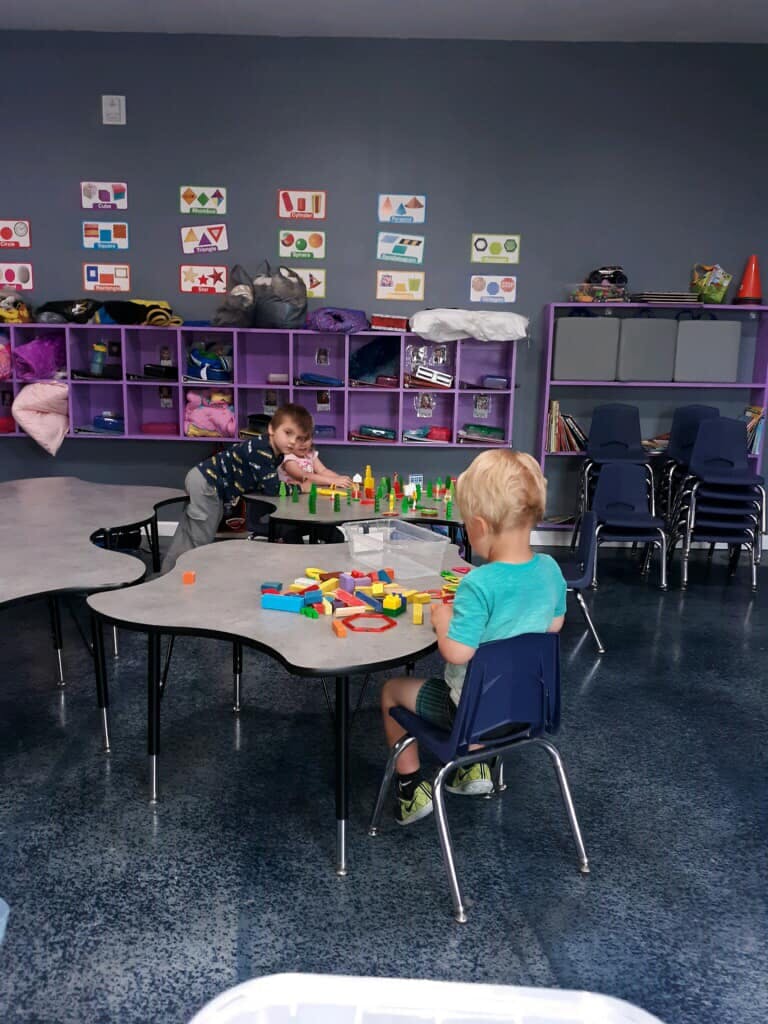 Two children playing with blocks at tables in a classroom