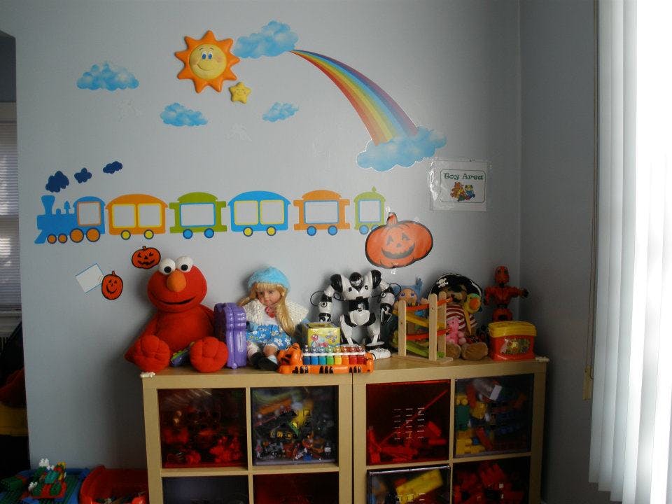Wall decorated with sun, rainbow, and train decals above a shelf of toys