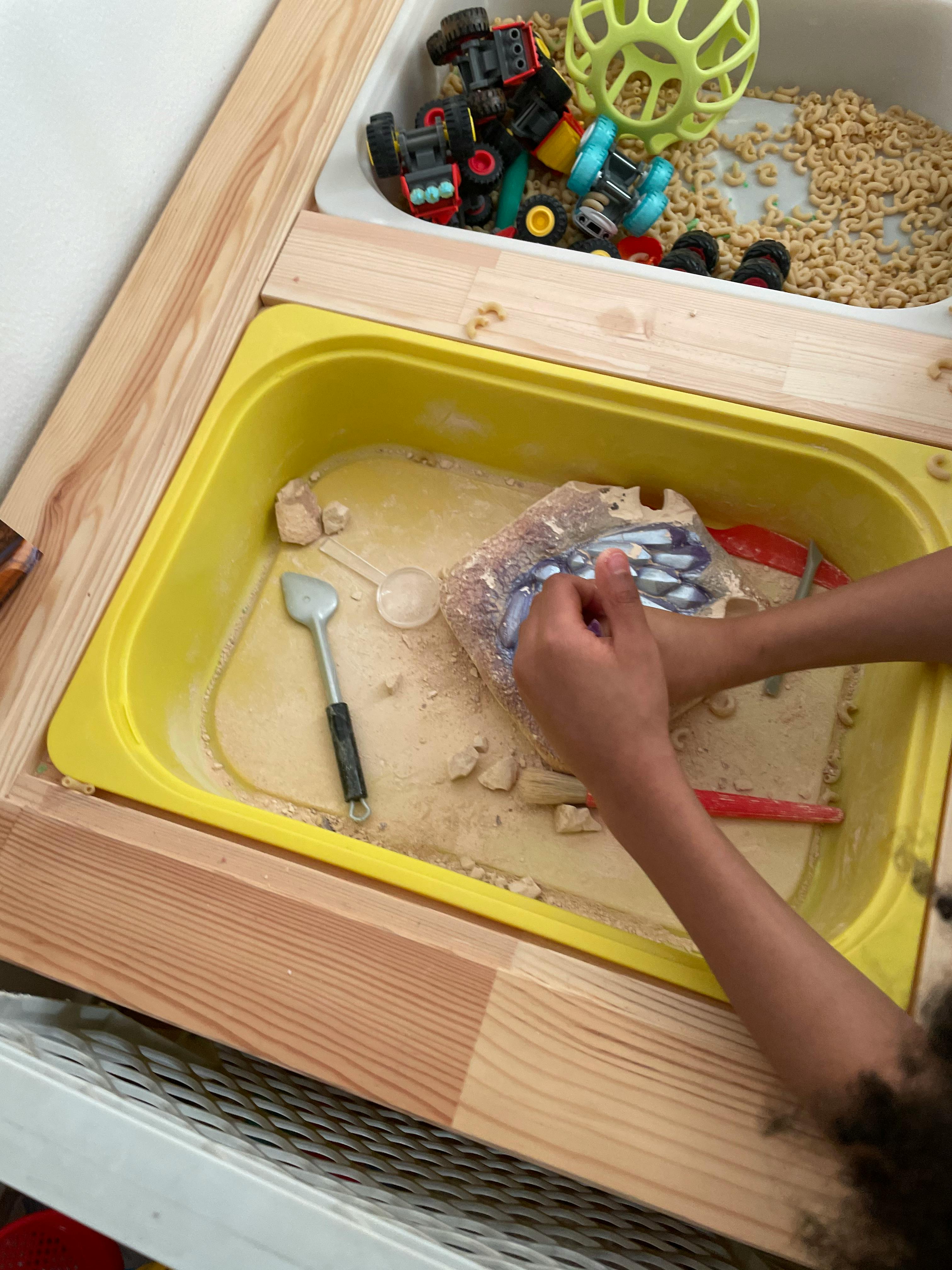 Child's hands playing in a yellow sand tray with a toy