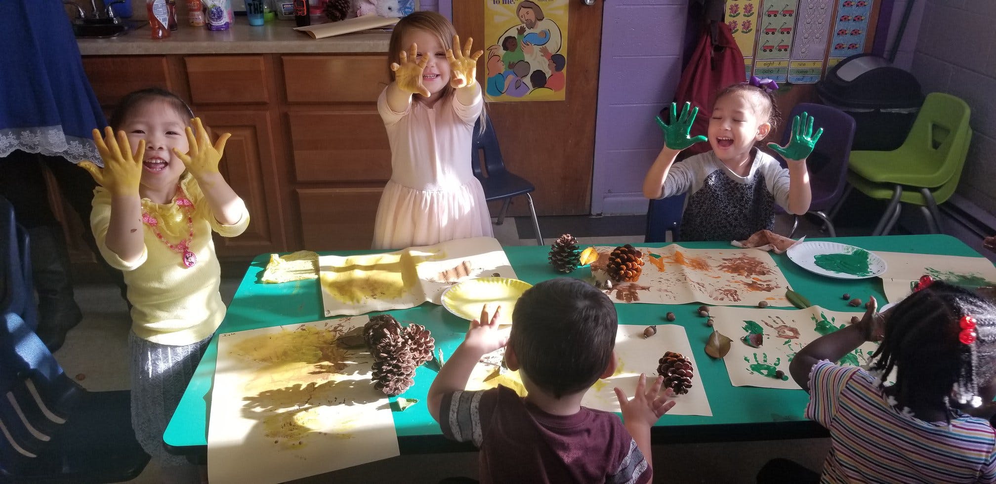 Children with painted hands at a table with pinecones and paper
