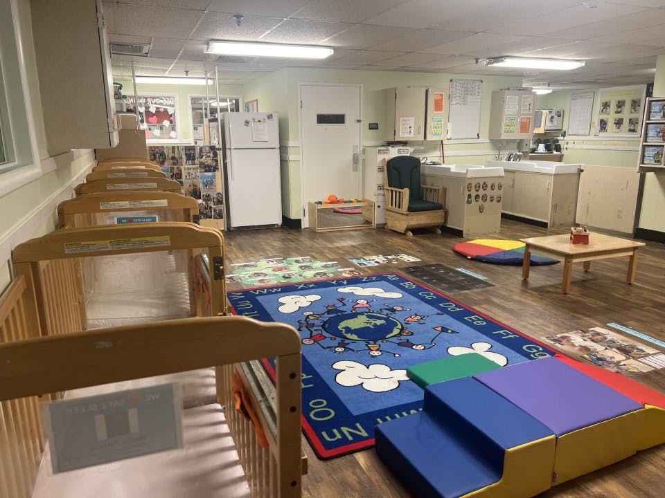 Cribs lined up in a daycare room with a play mat and changing tables