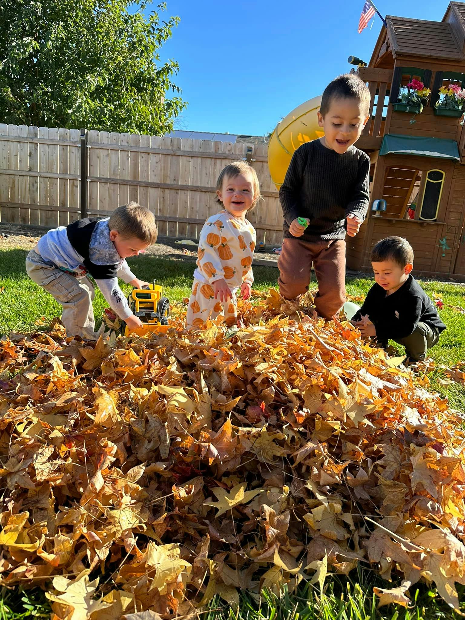 Four children playing in a large pile of autumn leaves