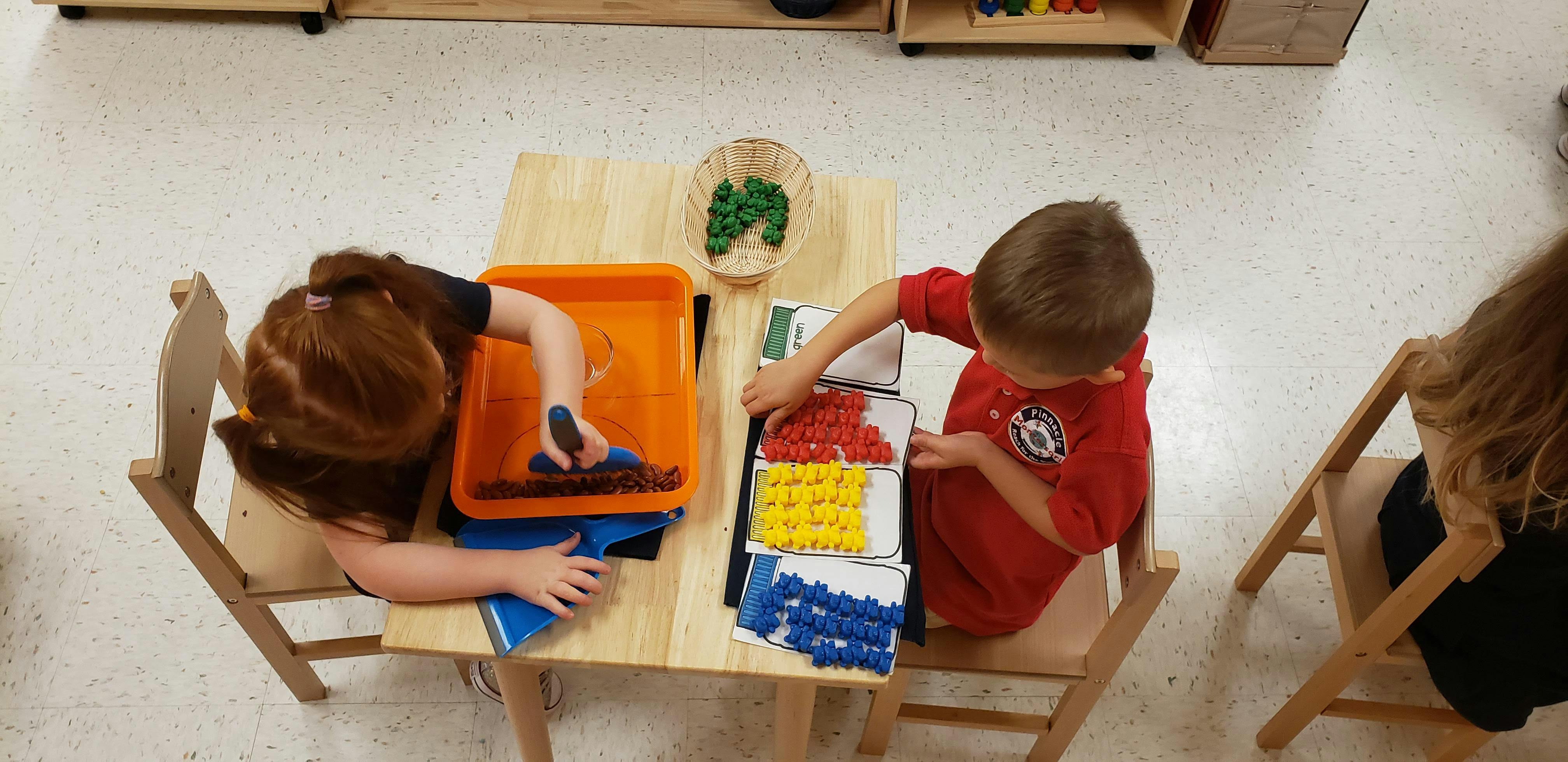 Two children at a table playing with colorful blocks and a tray