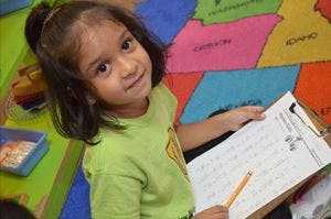 Child holding a clipboard with paper and a pencil