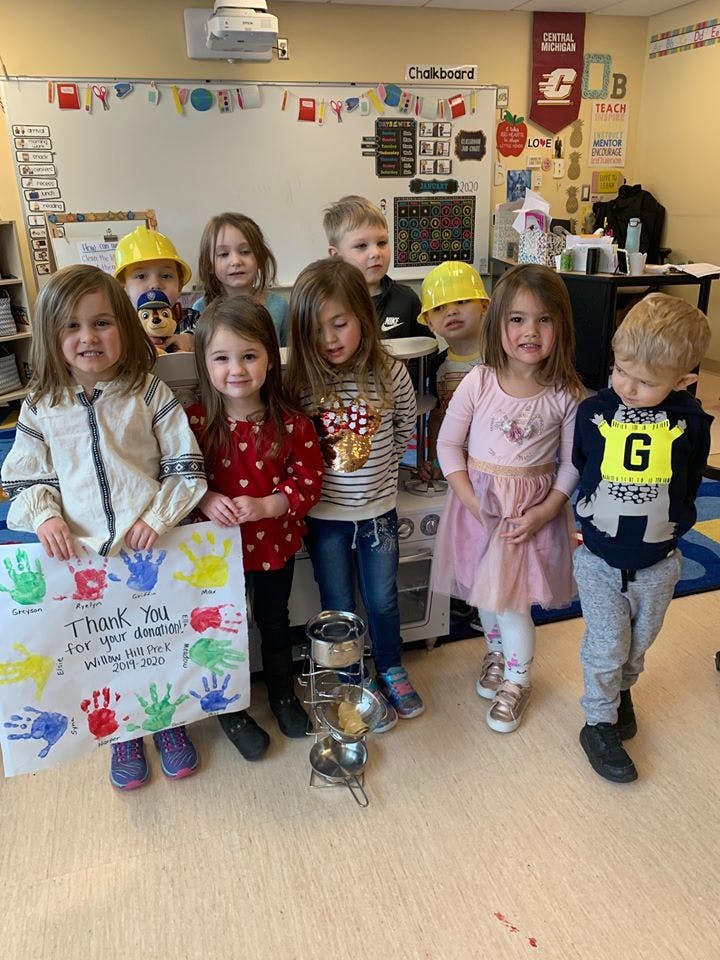 Group of children in a classroom, one holding a thank you sign
