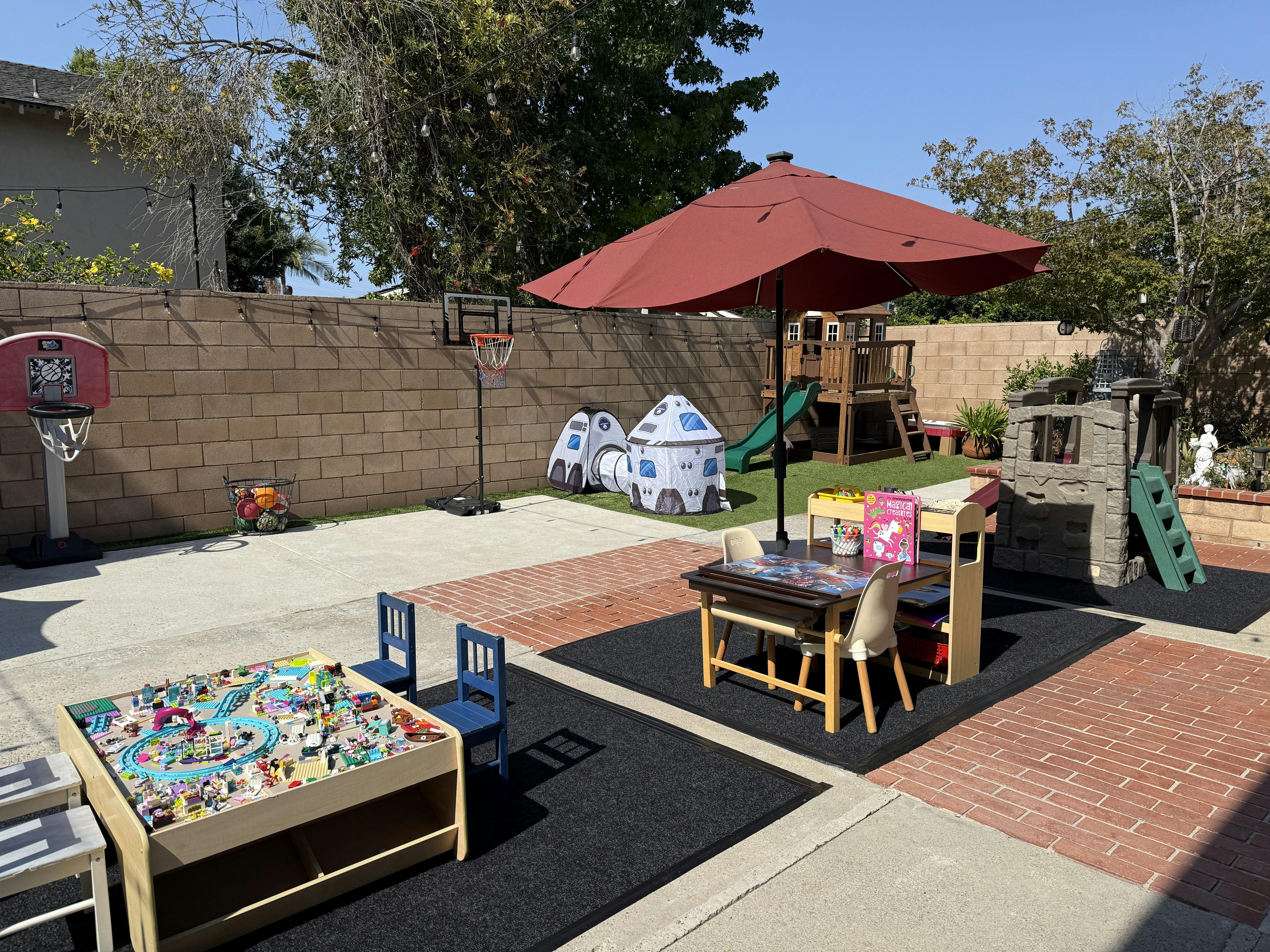 Outdoor play area with toy tables, a small slide, and a play tent