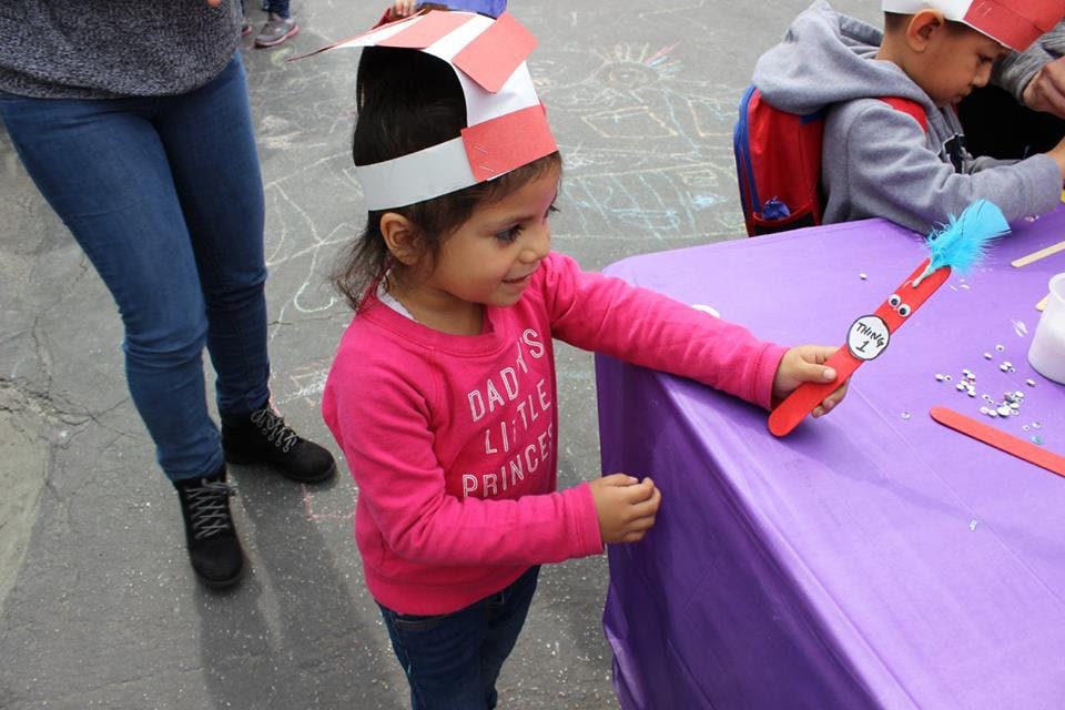 Child in a paper hat holding a craft stick with a blue pom-pom