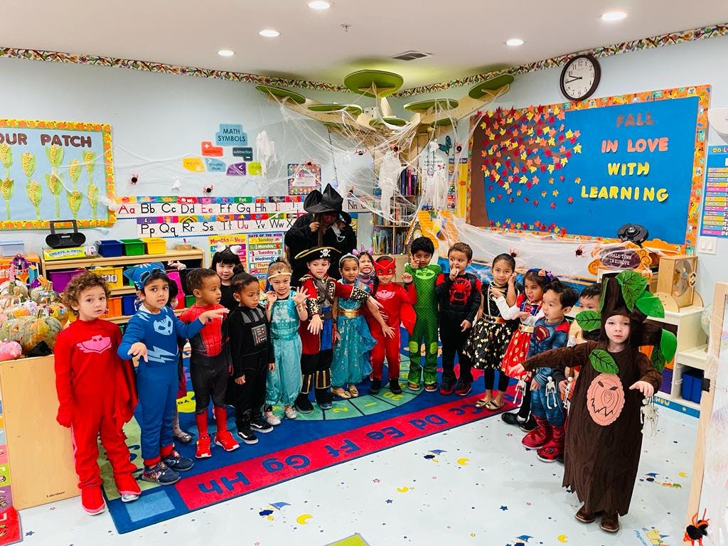 Group of children in various costumes standing in a classroom with Halloween decorations