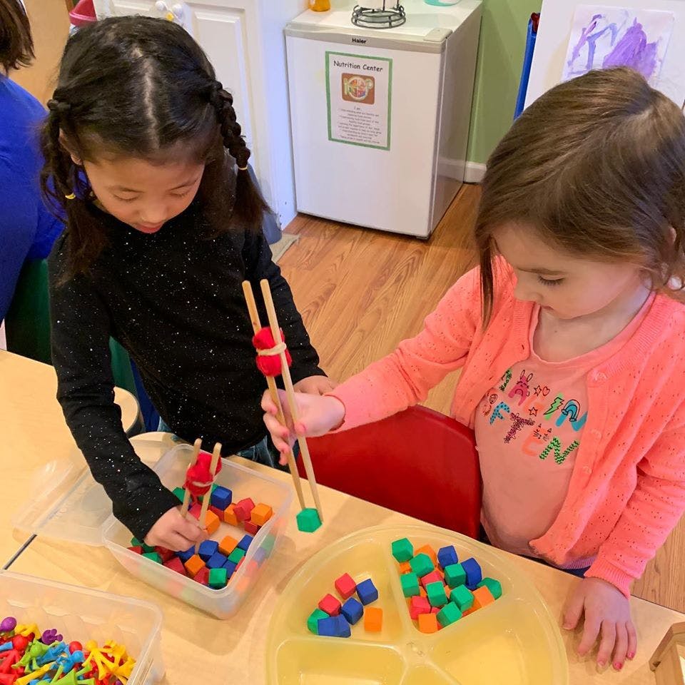 Two children playing with colorful blocks and tongs at a table