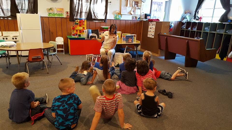 Adult reading to a group of children sitting on the floor in a classroom