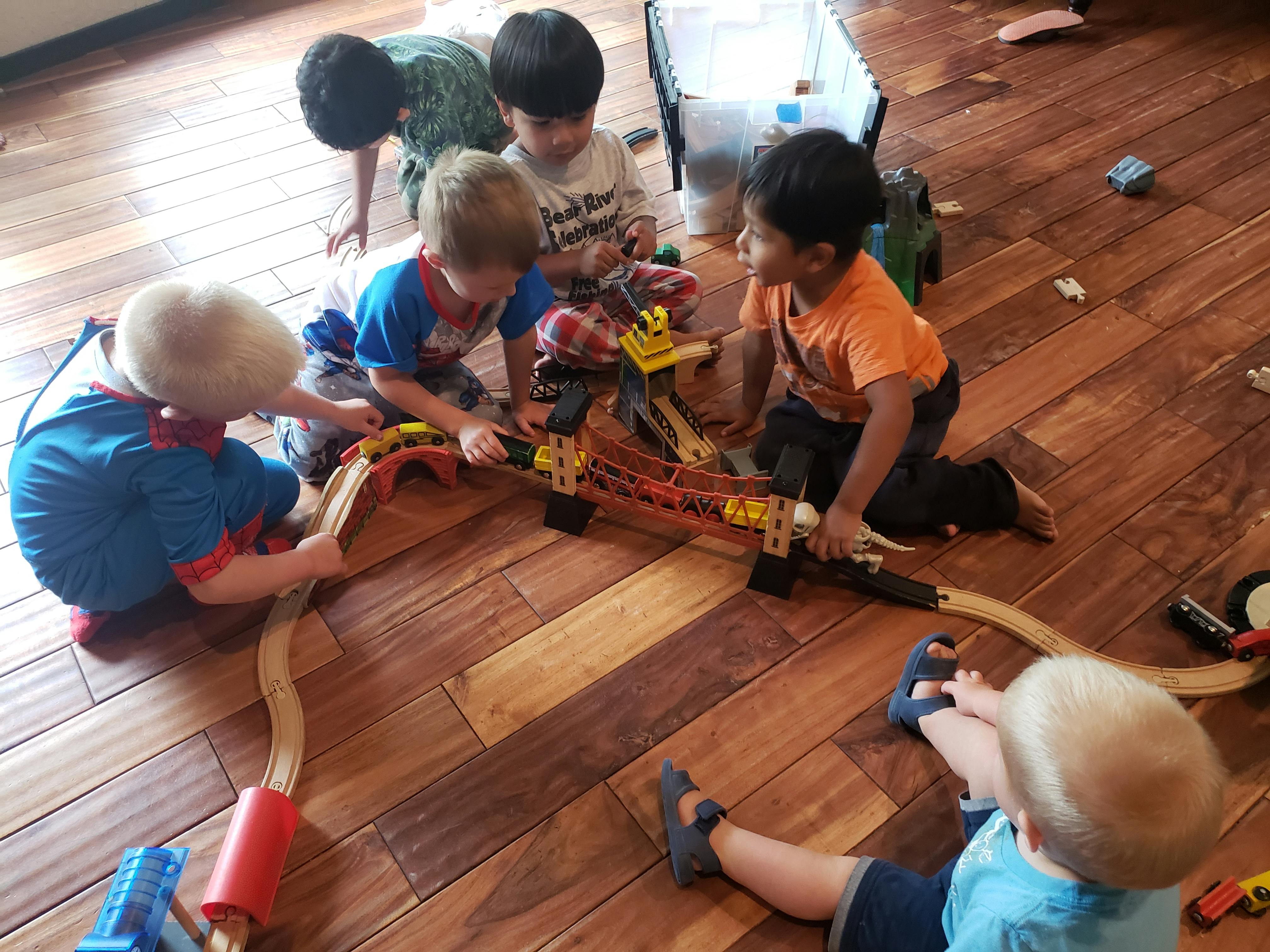Children playing with a toy train set on a wooden floor