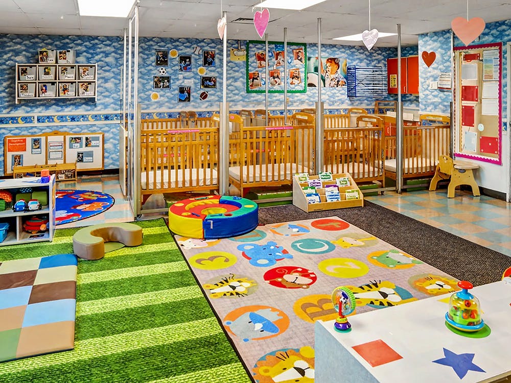 cribs in a daycare room with playmats and toys