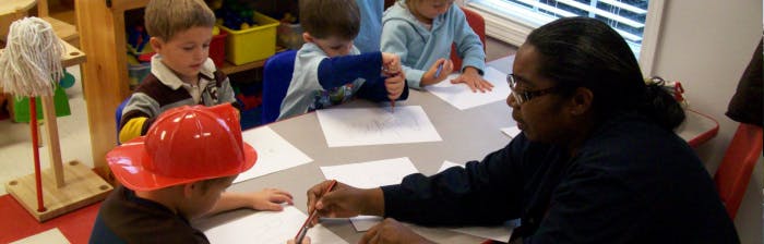 Adult and children drawing at a table in a classroom