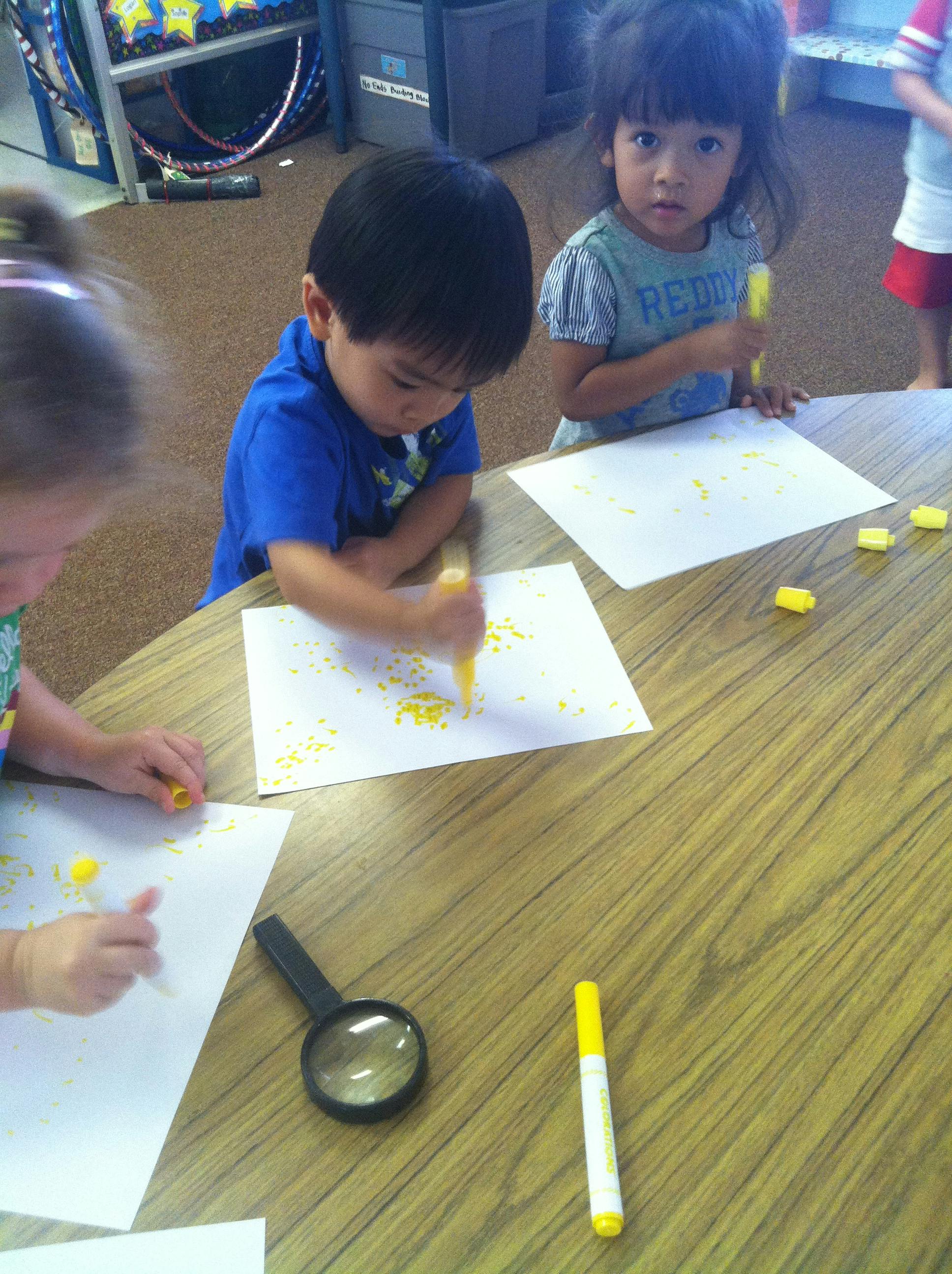 Children drawing on paper with yellow markers at a table