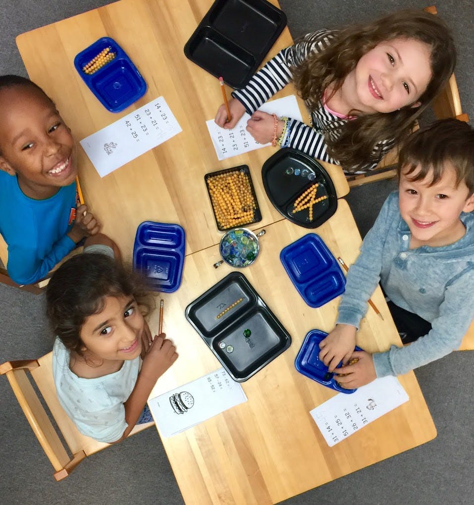 Four children sitting at a table with school supplies