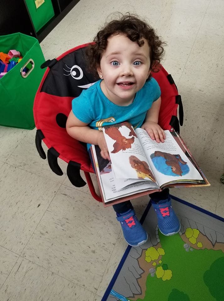 Child sitting in a ladybug chair holding an open book