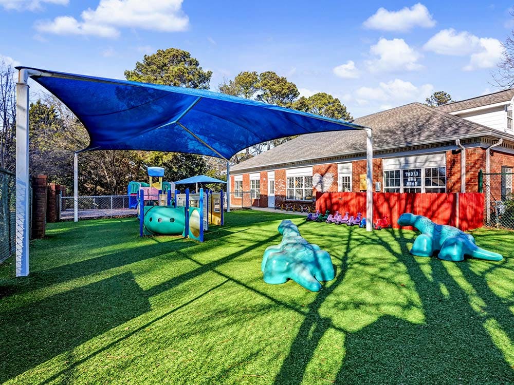 Outdoor playground with artificial turf, blue shade, and colorful play structures