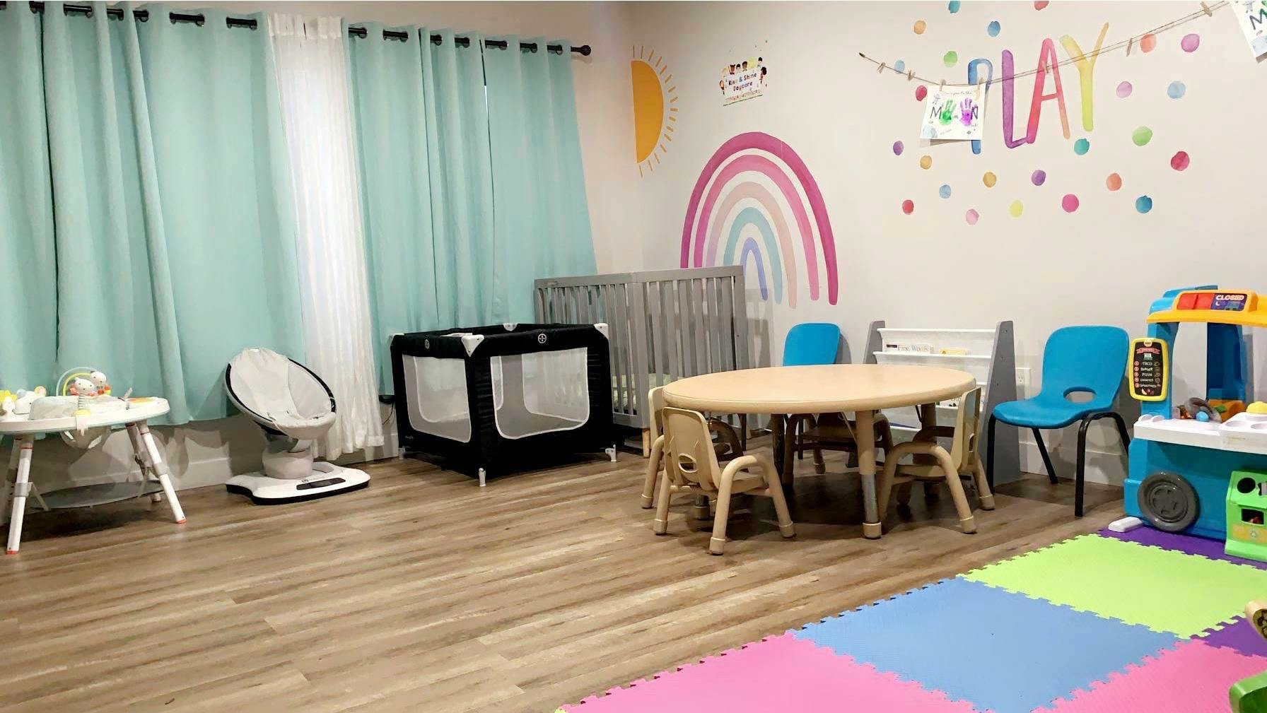 Childcare room with cribs, playpen, small table and chairs, play kitchen