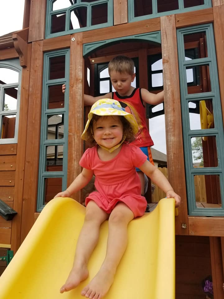 Child on a yellow slide with another child in a playhouse behind