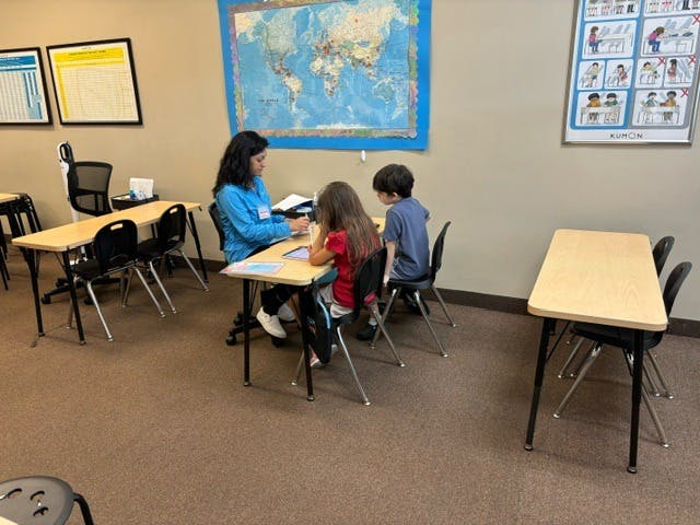 Adult and two children sitting at desks in a classroom