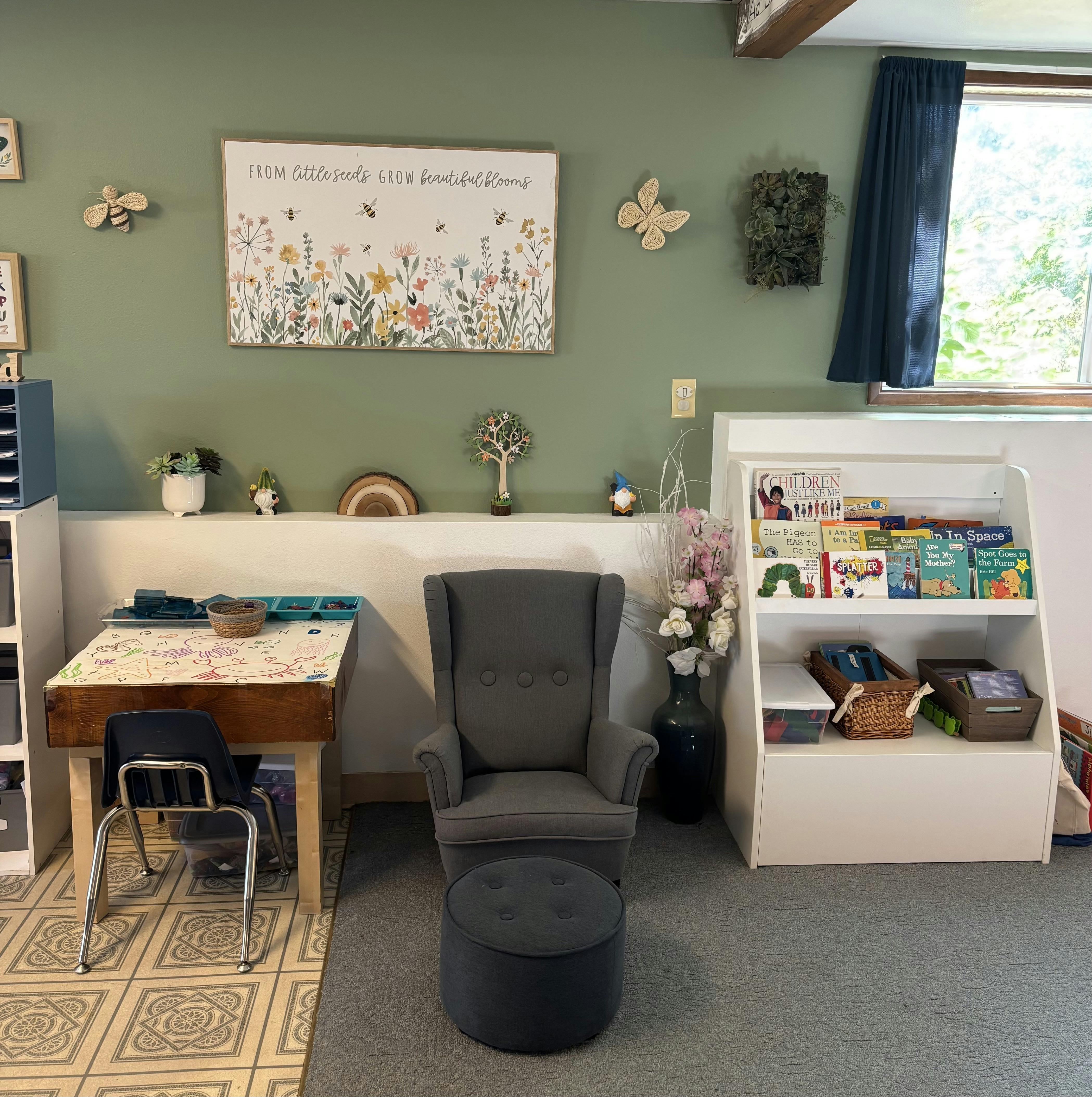 A classroom reading corner with an armchair, stool, child table, and bookshelf