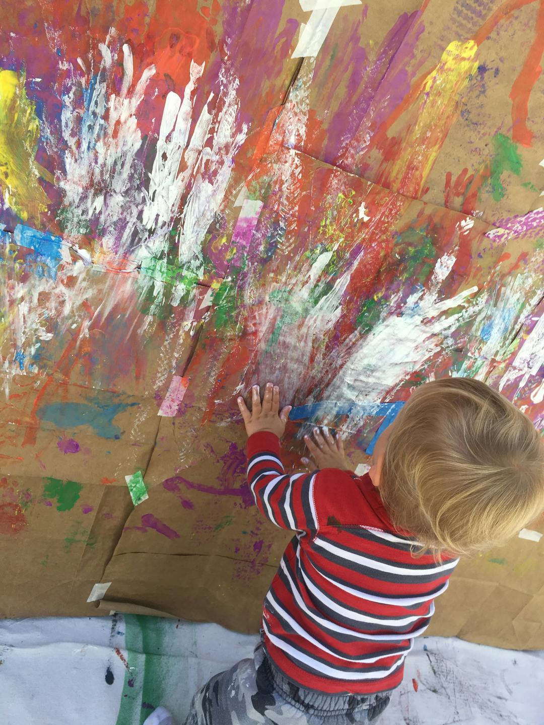 Child with hands on a large piece of cardboard covered in colorful paint