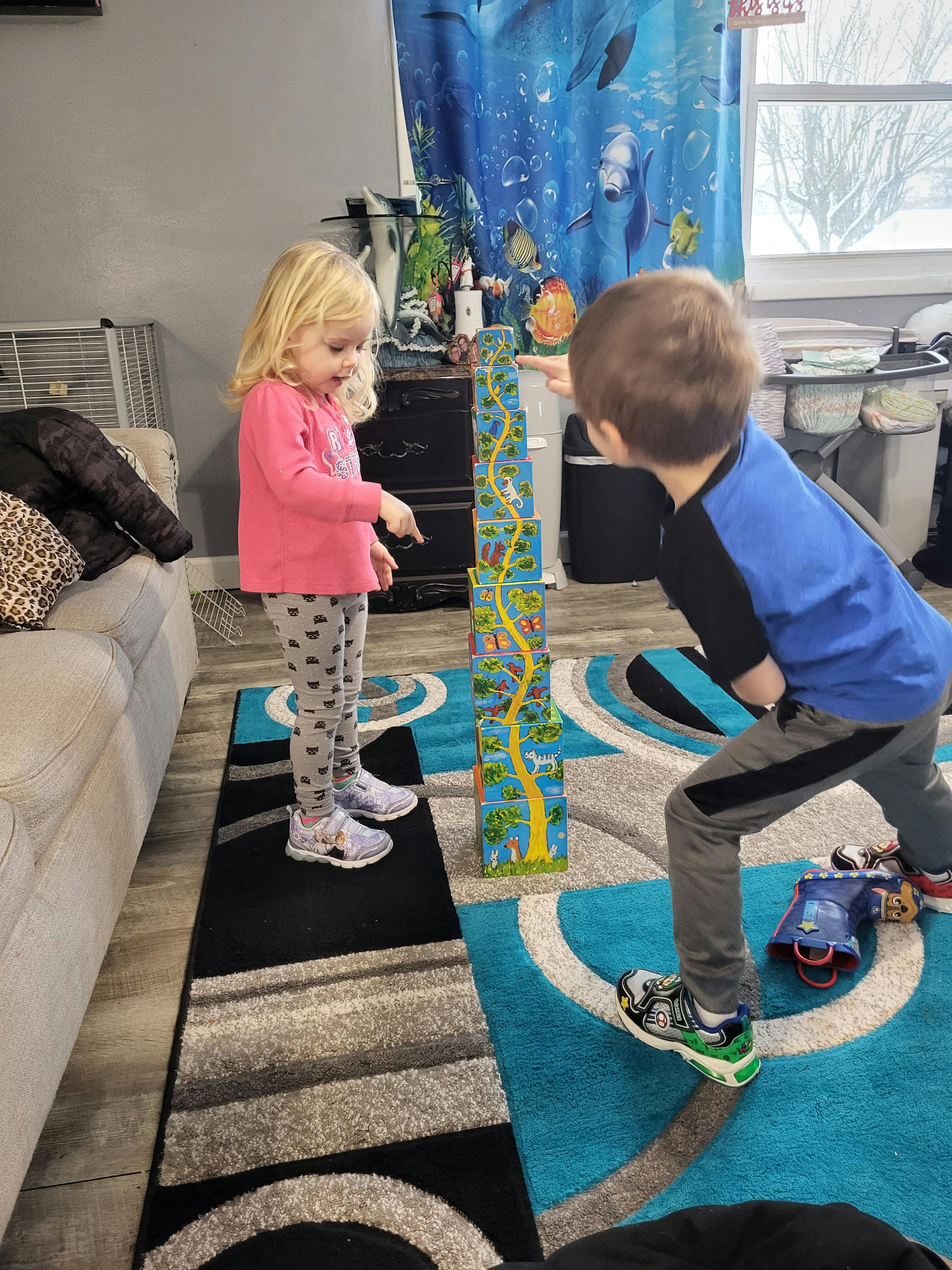 Two children playing with a tall stack of blocks