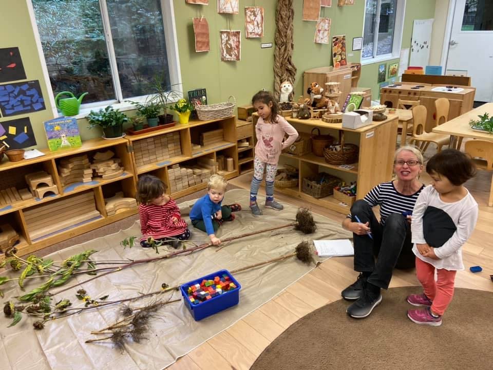 Adult and three children playing with branches and pinecones in a classroom
