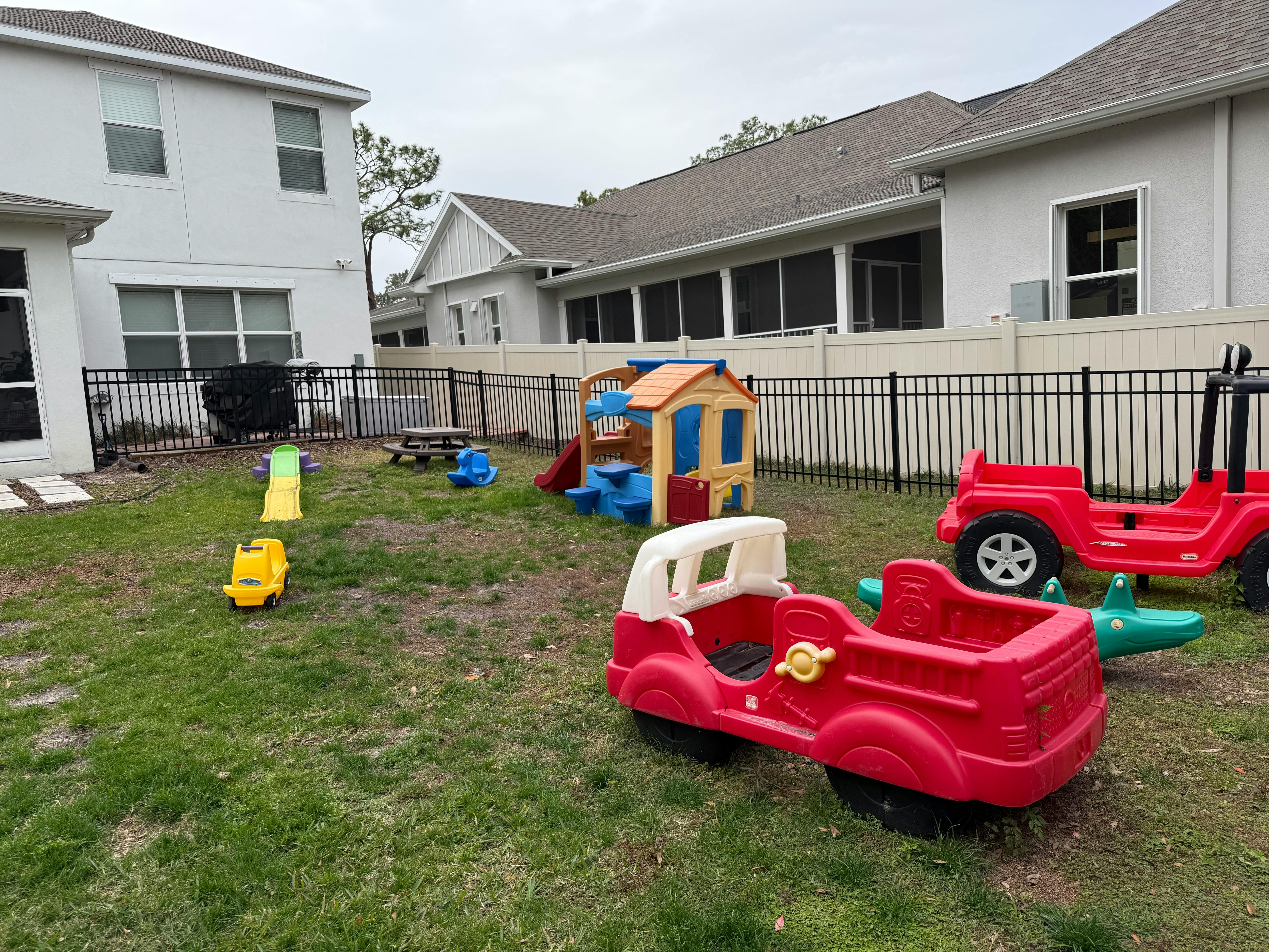 Playground with toy cars, slide, and playhouse in a grassy yard