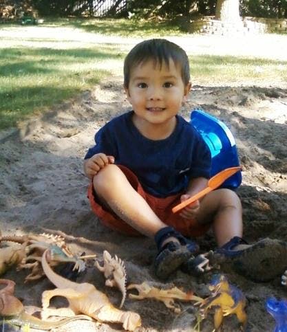 Child sitting in sand with a shovel and dinosaur toys