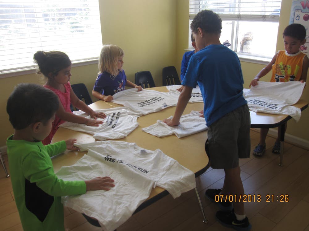 Children folding white t-shirts on a table