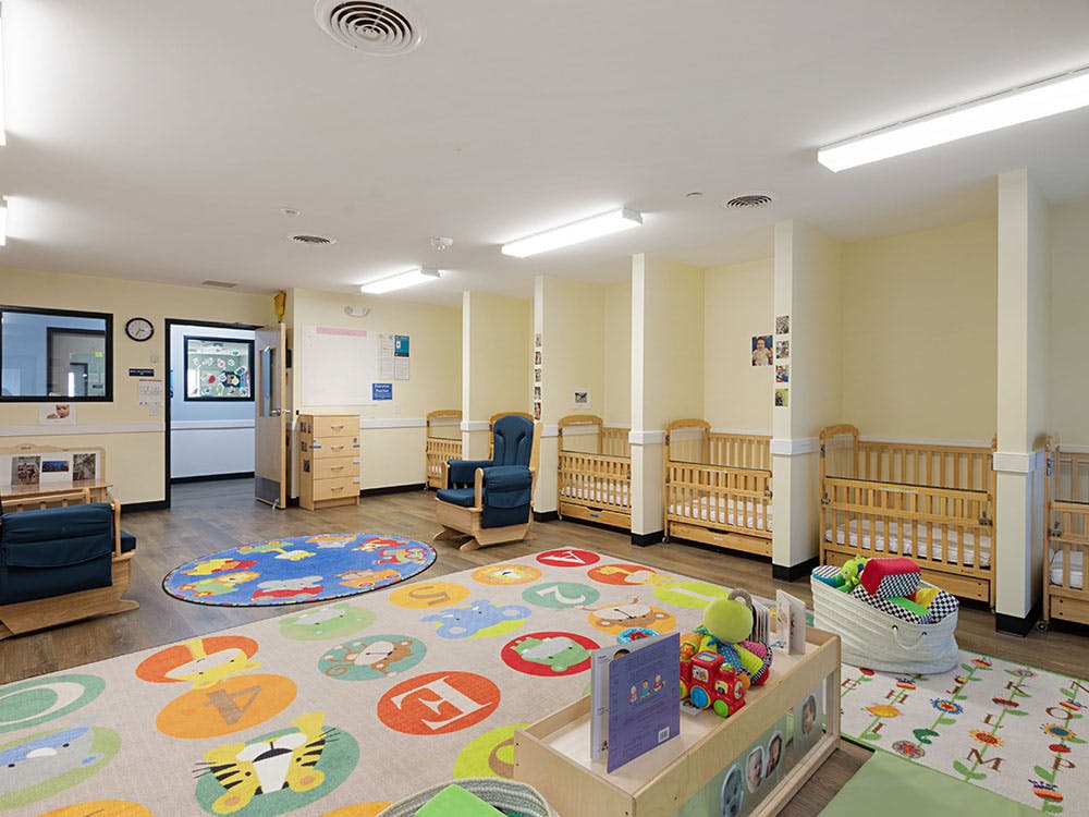 An empty nursery room with cribs, colorful rugs, and a rocking chair