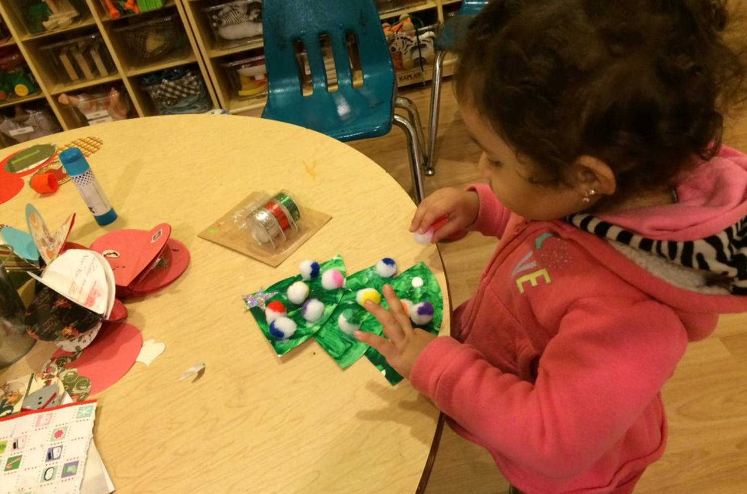 Child decorating a craft Christmas tree with pom-poms