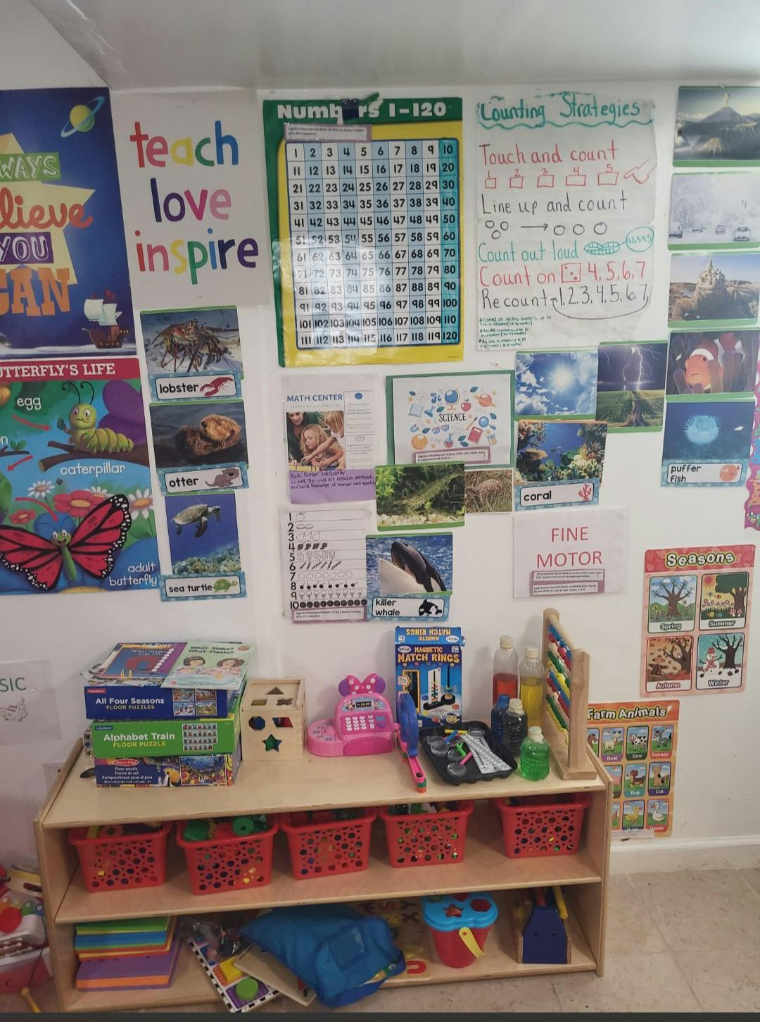 Classroom wall with educational posters, a toy shelf with puzzles, and baskets