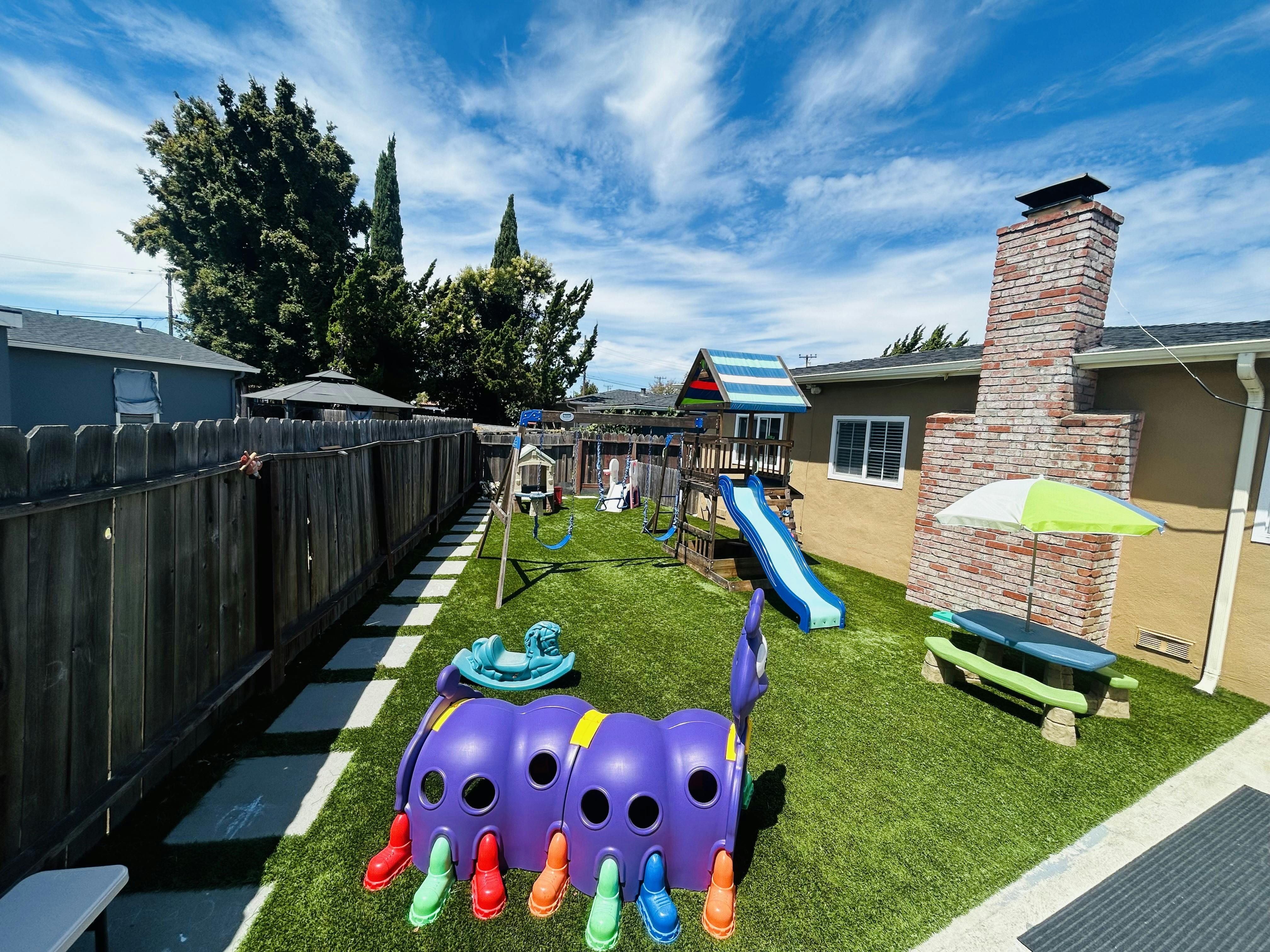 Backyard playground with slide, swings, and a tunnel toy on artificial grass