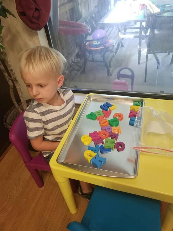 Child sitting at a table with colorful letter magnets on a tray