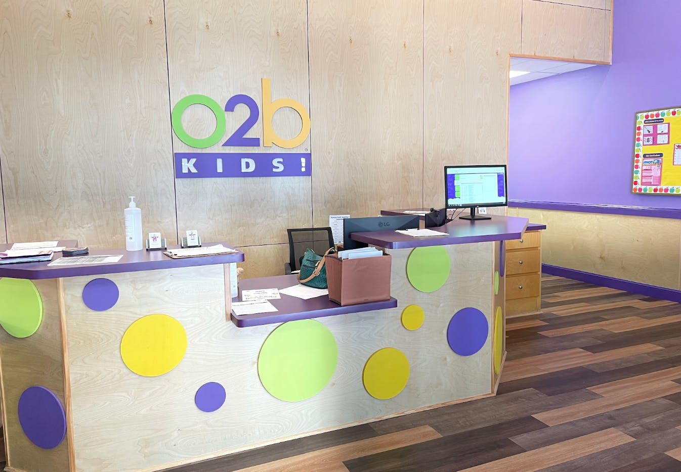 Reception desk with colorful circles and the O2b Kids! logo on a wooden wall