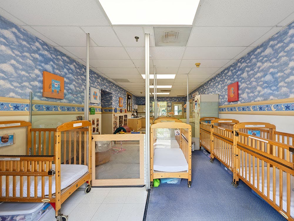 Rows of wooden cribs in a daycare room with cloud wallpaper