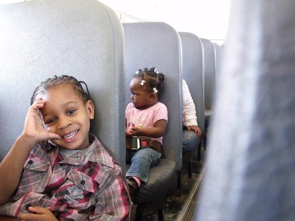 Child smiling at camera, another child looking away on a bus